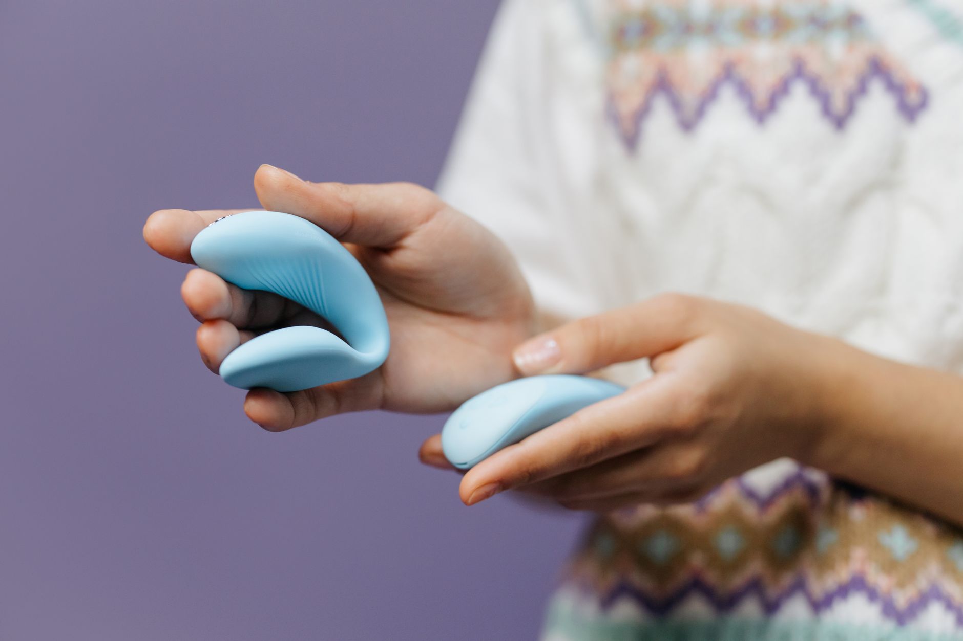 Primo piano delle mani che tengono un vibratore blu elegante su sfondo viola