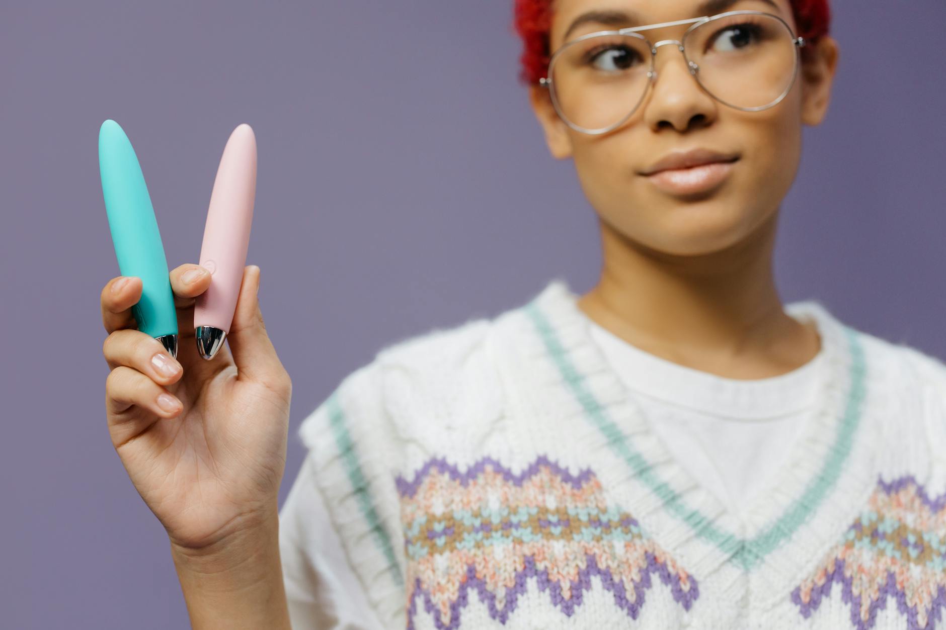 Woman holding colorful clitoral vibrators against a purple background