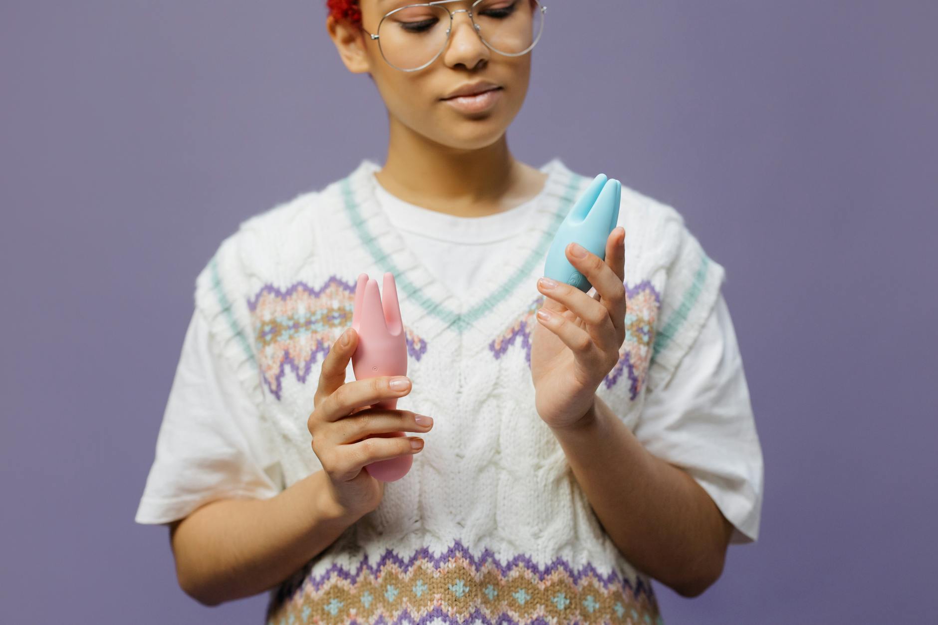 Woman holding blue and pink silicone vibrators in a contemplative manner.