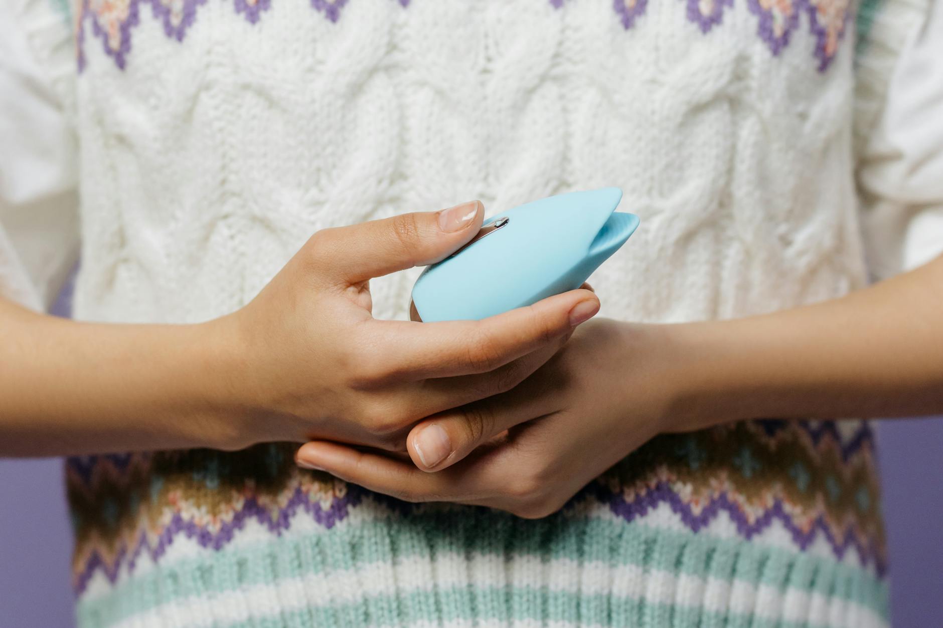Close-up of hands holding a lemon clitoral vibrator against a knitted sweater