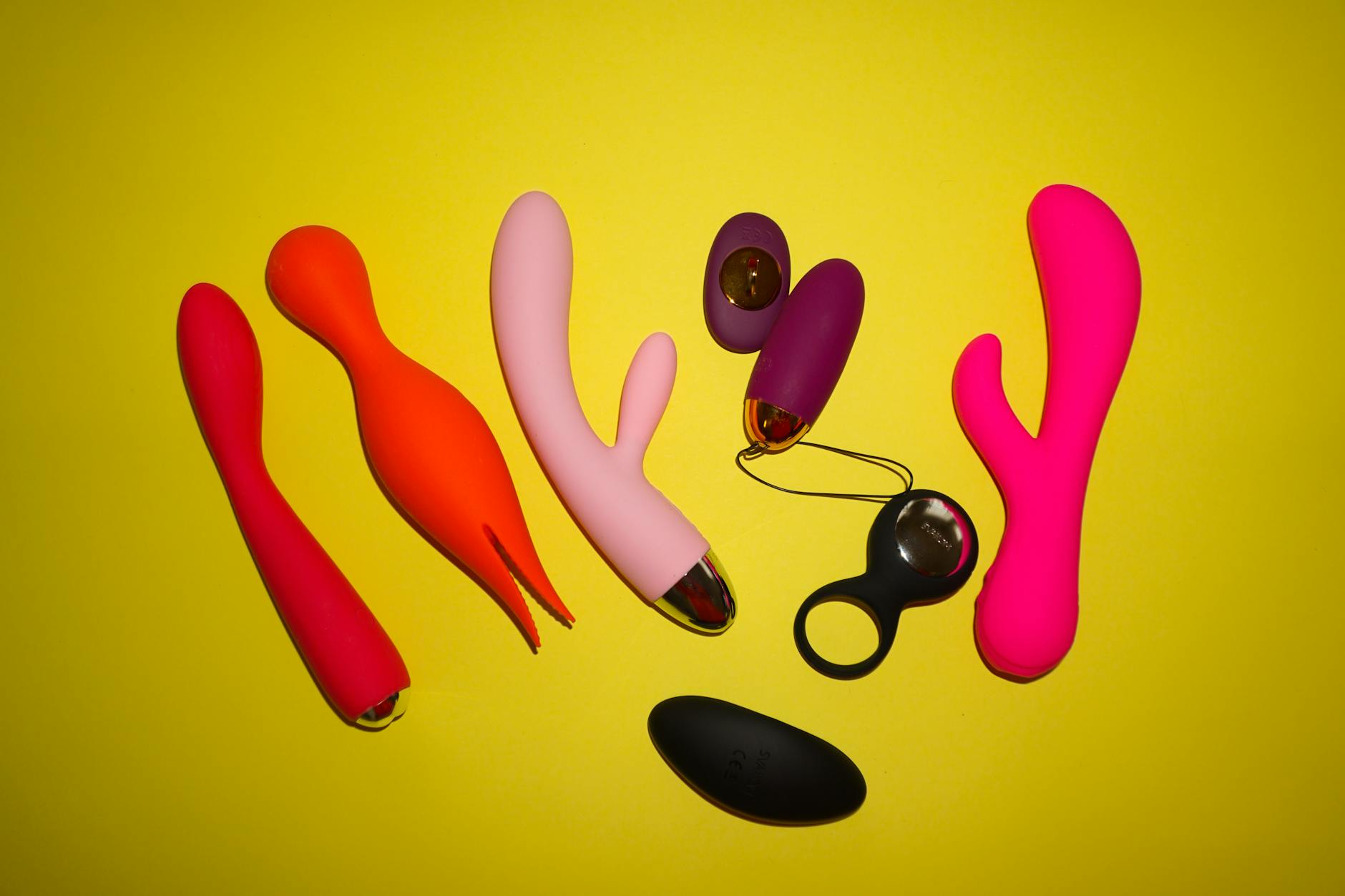 Colorful sex toys and vibrators displayed on a bright yellow background showing different shapes and styles